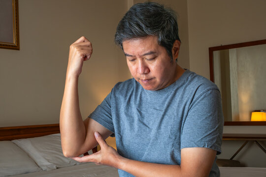 Senior man touching elbow with discomfort, calm bedroom background highlights joint stiffness for medical recovery theme.