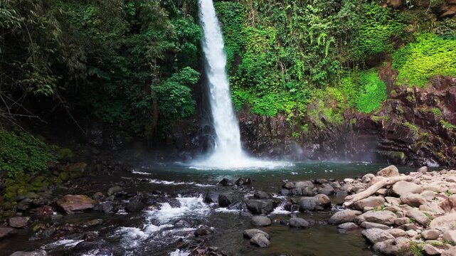 Aerial view of a waterfall cascading through basalt columns. Water plunges into a deep, narrow gorge. Rugged, jagged cliffs frame the falling stream. Exposed earth and stone surround the dramatic drop