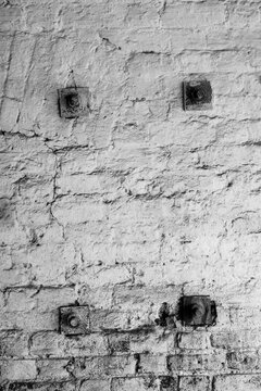 An old roughly plastered, sooty brick wall with metal squares