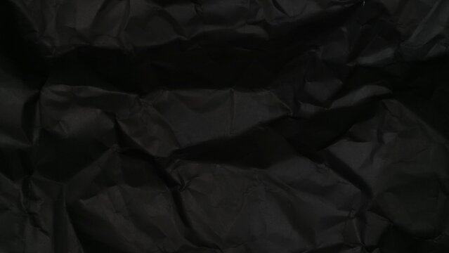 Abstract background texture of dark black crumpled paper with soft shadows.