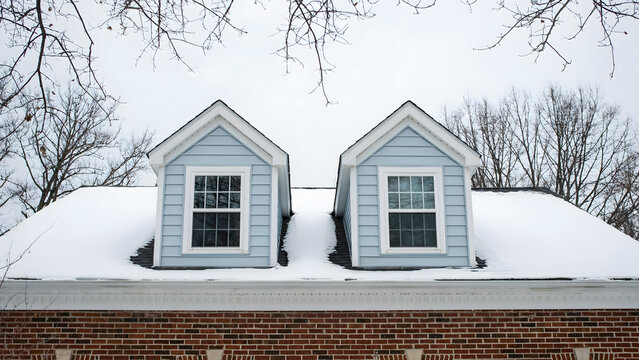 Two light blue wooden dormer windows on a snowy roof with brick exterior
