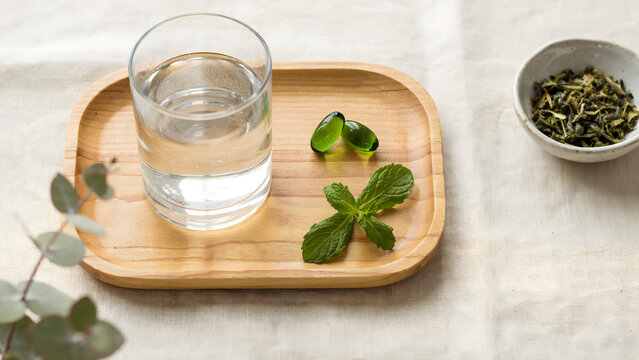 Glass of water with green herbal leaves and capsules on a bamboo tray
