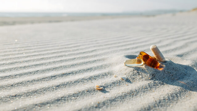 A pair of medication pills lying on the textured sand of a bright beach