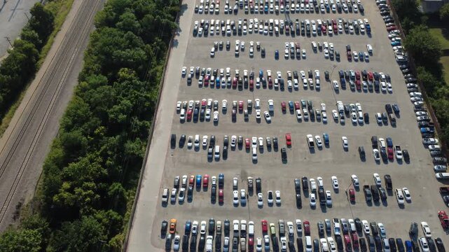 Ordered rows of parked vehicles fill expansive paved holding lots next to mature woodland canopies showcasing commercial organization. Staging operations occupy storage infrastructure, Irving, TX