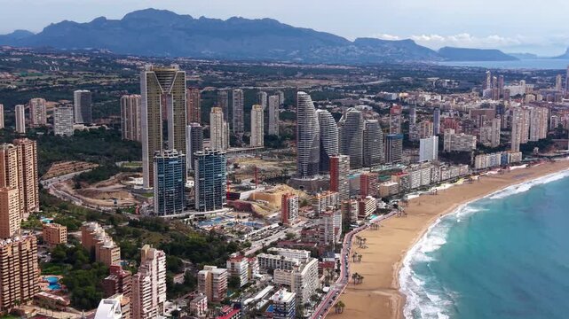 Aerial view of Benidorm, Spain showing iconic skyscrapers, sandy beach, turquoise Mediterranean Sea, and mountain backdrop on the Costa Blanca