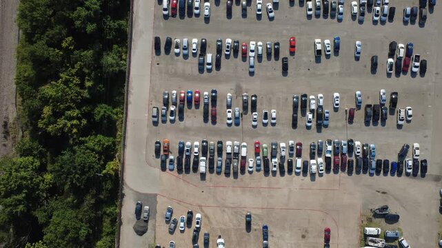 Fenced perimeter lines enclose structured rows of automobiles situated near dense tree lines reflecting intensive facility space utilization. Automotive storage operations continue in Irving, TX