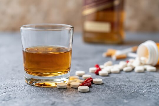 The Whiskey Glass with Pills and Bottle in Background on Concrete Surface