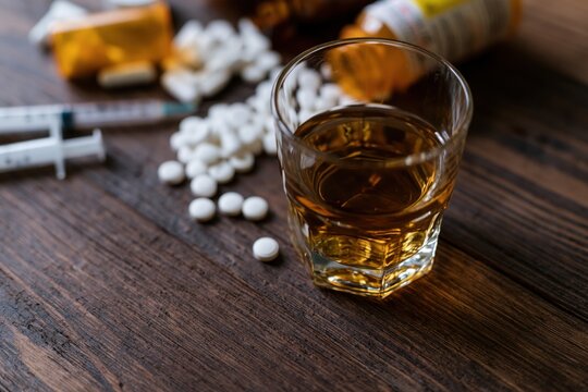 The Glass of Whiskey Amidst Pills and Syringe on Dark Wood Table