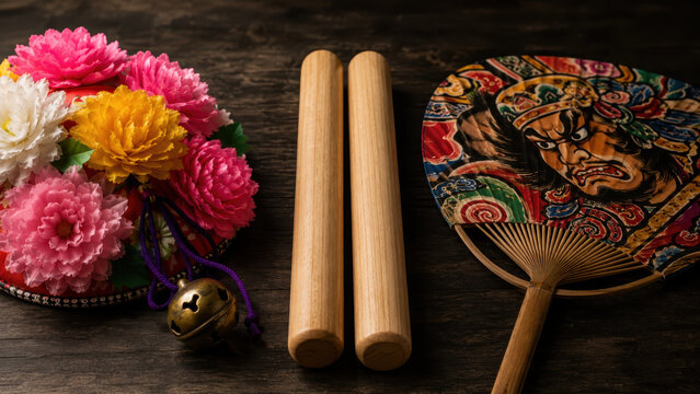 Aomori nebuta festival props on dark wooden table, colorful floral hanagasa hat, taiko drum sticks, painted warrior fan, brass bell, japanese summer parade culture, lantern float celebration