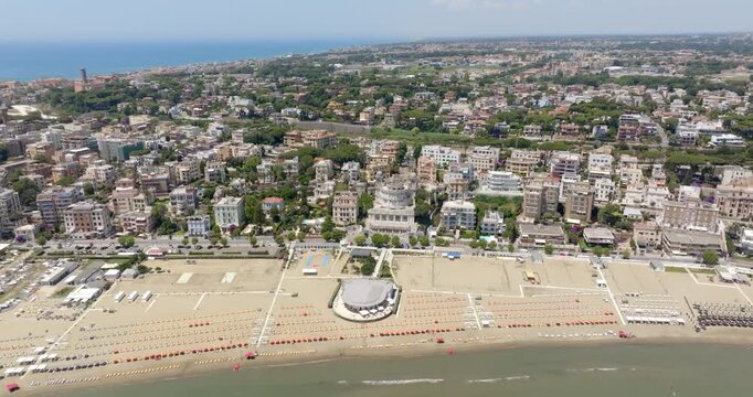 Aerial view of Anzio, in Lazio, Italy. It's a coastal city featuring a busy harbor, sandy beaches, and urban buildings along the shore under a clear sky, capturing an ideal summer destination.