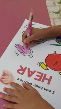 Child coloring a hearing-themed activity sheet with a pink marker