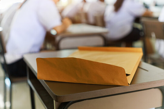 Examination concept: Test paper packet on desk with students studying in classroom.