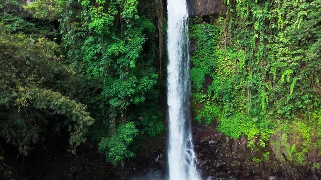 Aerial view of a waterfall cascading through basalt columns. Water plunges into a deep, narrow gorge. Rugged, jagged cliffs frame the falling stream. Exposed earth and stone surround the dramatic drop