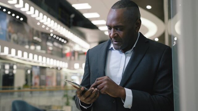 Thoughtful puzzled mature African American business man with mobile phone think in office pensive concentrated adult businessman male entrepreneur executive with smartphone thinking pondering idea