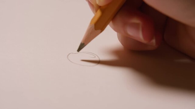 Close-up of a hand delicately drawing a small circle with a yellow pencil on plain paper, showcasing artistic precision and the creative process.
