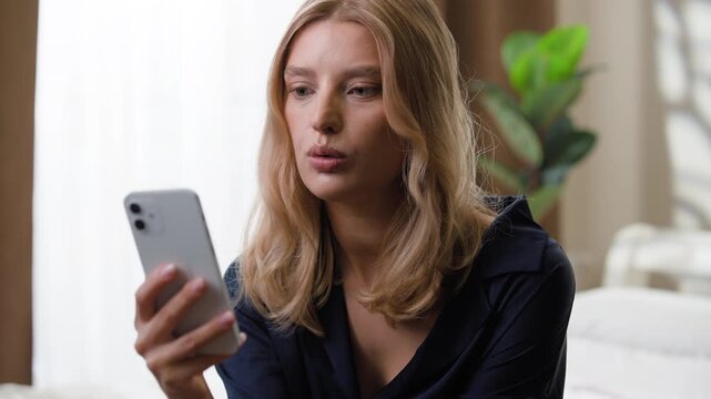 Gadget addicted shocked amazed Caucasian woman using mobile phone watching shocking video content close mouth female girl with smartphone astonish with bad online news notification at home bedroom