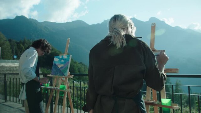 Caucasus mountains. Students who came on vacation devote time to their hobby - drawing. Easel with watercolor painting on the ion of rocks and sky