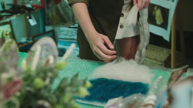 Girl plucks off pieces of wool for basis of felted product. Homecraft studio hobby interior. Work table covered with bubble wrap in workshop
