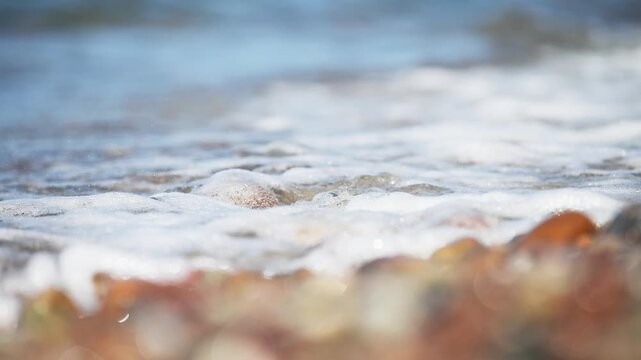 Colorful sea pebbles washed by gentle ocean waves on rocky shore under natural daylight