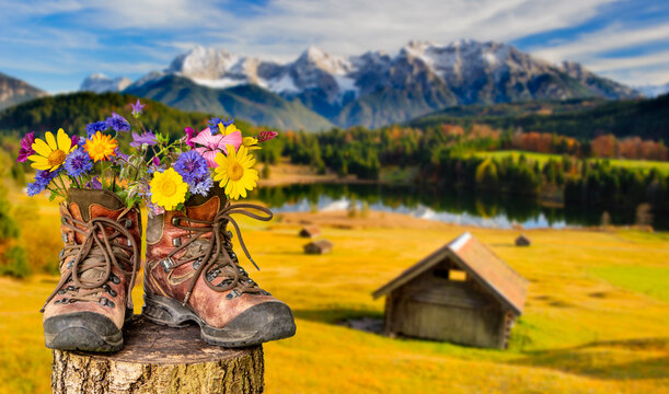 Ein Paar Wanderstiefel gef&uuml;llt mit einem Strau&szlig; Blumen, steht auf einer Almwiese vor dem Bergpanorama des Karwendelgebirges - FOTOMONTAGE
