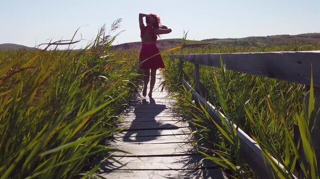  Red haired woman in red skirt dancing on wooden footbridge in reed