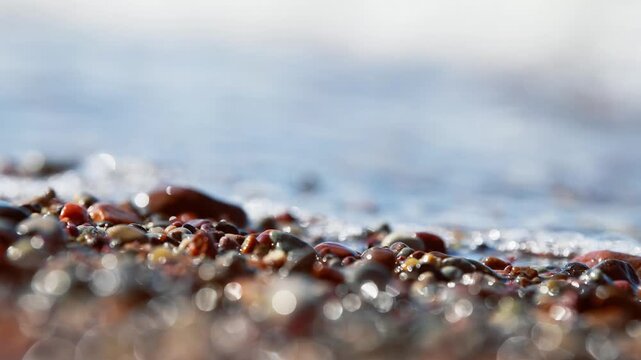 Close up of sea foam and wet pebbles on sandy shore with soft natural light
