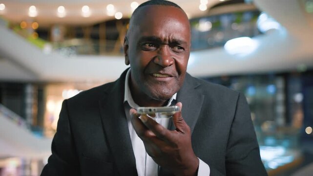 Excited smiling happy mature African American business man recording audio message with mobile phone easy command app businessman male specialist smile record voice mail communicate with smartphone