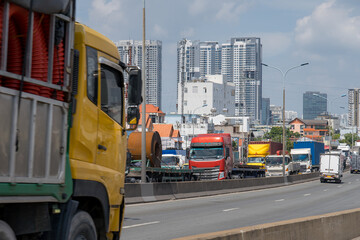 Fototapeta premium Cargo Trucks on a Busy Highway with Ho Chi Minh City Skyline