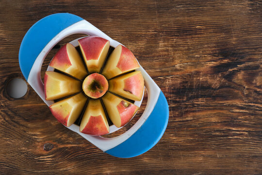 Top view red apple sliced by blue apple slicer tool on wooden cutting board background.