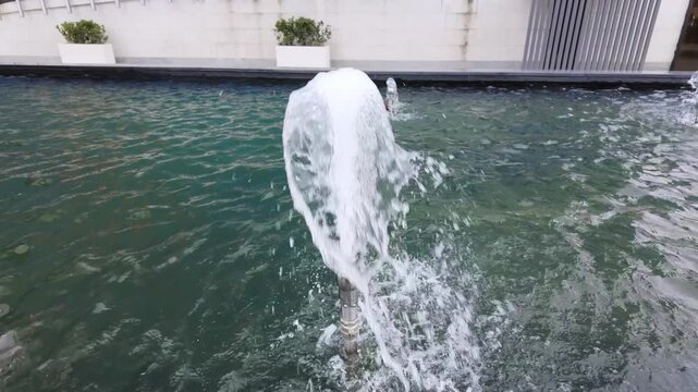 Close-up of a bubbling fountain jet splashes upward from a calm turquoise pool.