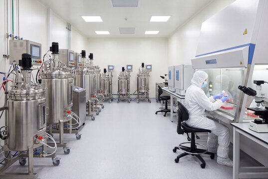 Modern biotechnology laboratory with bioreactors, scientist in protective suit working in a biosafety cabinet.