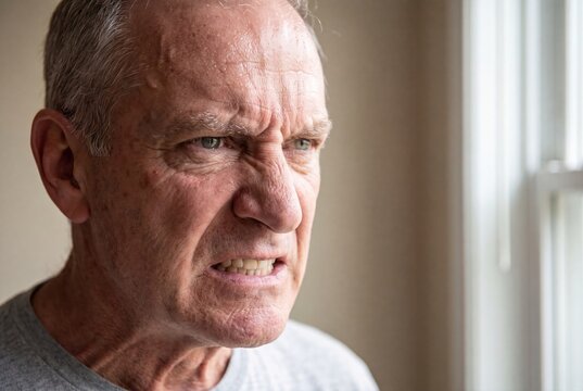 Close-up portrait of an angry elderly man with furrowed brow and clenched teeth, expressing frustration and rage.
