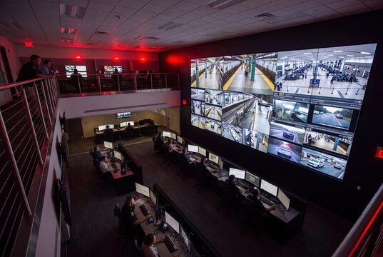 Modern security operations center with a massive video wall displaying surveillance feeds from subway and traffic.