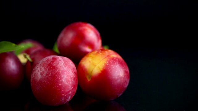 Natural fresh plums with green leaves on elegant black background