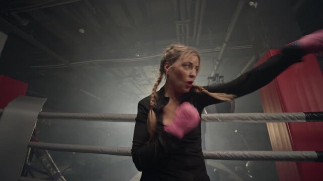 Young Caucasian woman shadow boxing inside ring, throwing punches with boxing wraps. Footage ideal for fitness brand advertisements, women empowerment campaigns and gym promotions