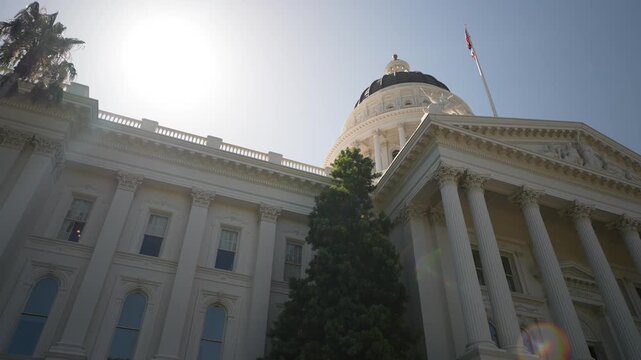 Views show the Capitol of California in Sacramento at sunrise with clear skies and bright light shining on the building