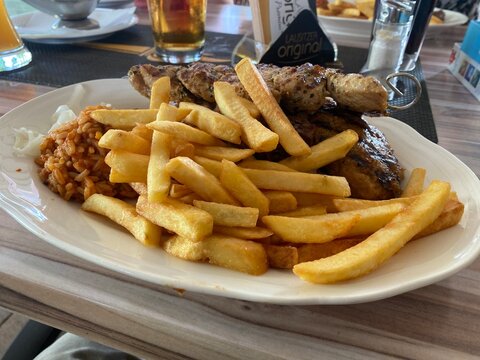 Herzhaftes Grillgericht mit Pommes frites, Fleisch und Ajvar auf einem Teller. Deftige Hausmannskost, Restaurantbesuch, Mittagessen, Abendessen und authentische Food-Fotografie.