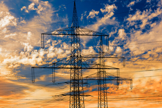 Die Strommasten einer Hochspannungsleitung stehen isoliert vor Himmel mit Wolken, FOTOMONTAGE