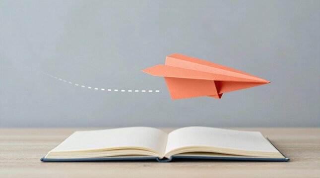 Paper plane flies over an open book on a wooden table