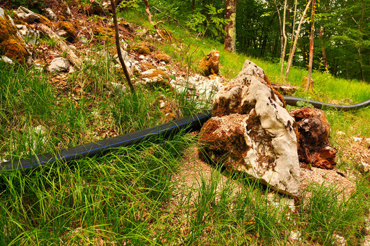 Black pipe next to a mossy boulder in Učka Nature Park, Croatia. Suitable for water management, rural infrastructure, nature vs technology concepts, and environmental studies.
