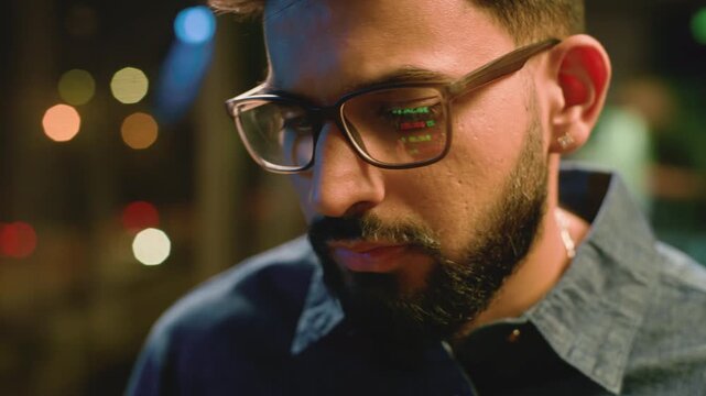 Indian business man using digital tablet device at night office lights reflection graph data reflect in glasses. Concentrated Arabian businessman male guy trader wear eyeglasses coding at evening