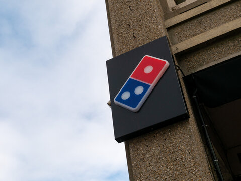 Low-angle shot of a Domino's Pizza logo sign mounted on the corner of a concrete building, photographed against a partly cloudy sky.