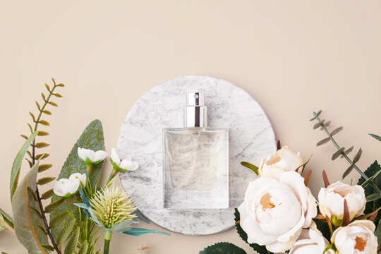 Perfume bottle on marble tray with decorative white roses and green leaves on a pastel beige background, copy space