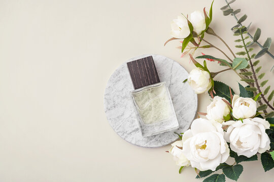 Perfume bottle with wooden cap on marble tray with white roses decoration on beige background, top view