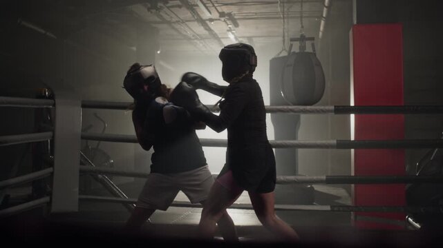 Two young Caucasian women sparring in boxing ring, wearing protective headgear and gloves. Clip is perfect for fitness apps, female empowerment videos, and gym promotional campaigns