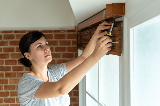 Woman installing window blinds carefully.