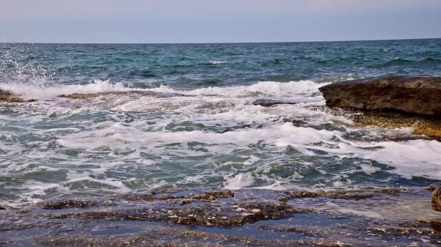 Waves crash against rocky shore, creating foam and splashes in coastal scene