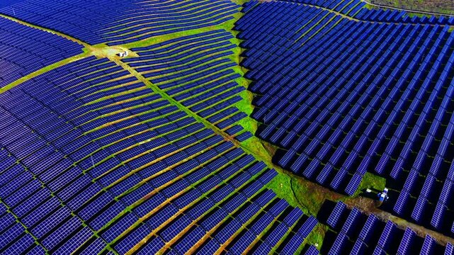Overhead pattern of solar panel rows across field. Diagonal lines of dark modules separated by strips of green grass.