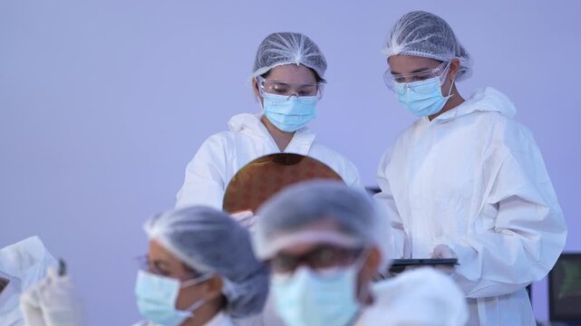 Semiconductor engineer inspects an iridescent silicon wafer against the light while holding a tablet during a quality check in a sterile hitech cleanroom manufacturing lab
