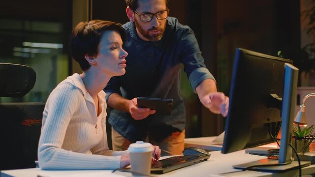 Caucasian business woman working with computer man boss coming dissatisfied talking leader checking bad work mistake talk arguing with businesswoman two colleagues argue at dark evening night office
